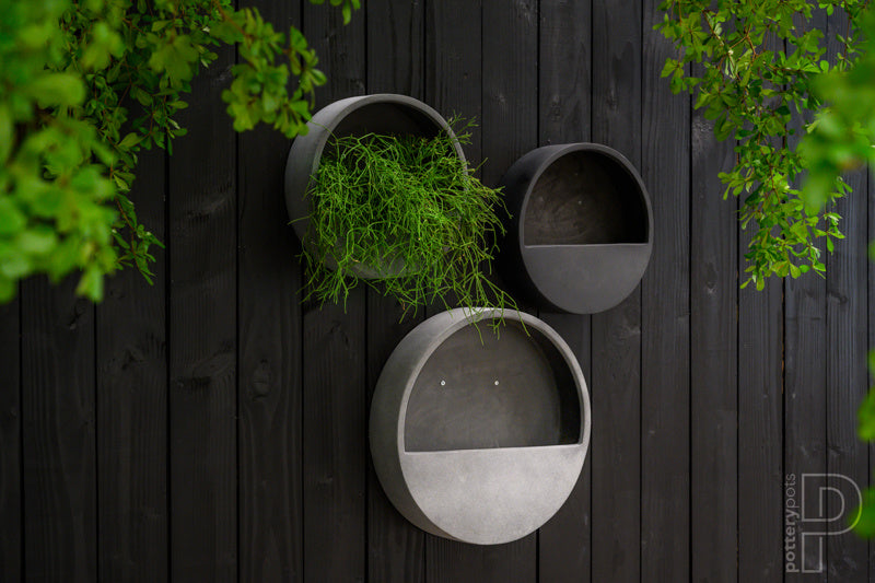 Een stijlvolle, ronde hangende bloempot van Pottery Pots, gemaakt van duurzaam fiberstone in een elegante grijze kleur. Perfect voor zowel binnen als buiten, ideaal voor het toevoegen van een groene touch aan muren zonder extra vloerruimte in beslag te nemen."