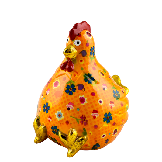 "Oranje keramische Pomme Pidou spaarpot kip Claire met bloemen- en taartjesprint. Een speelse en stijlvolle manier om geld te sparen, perfect als cadeau of decoratief item."